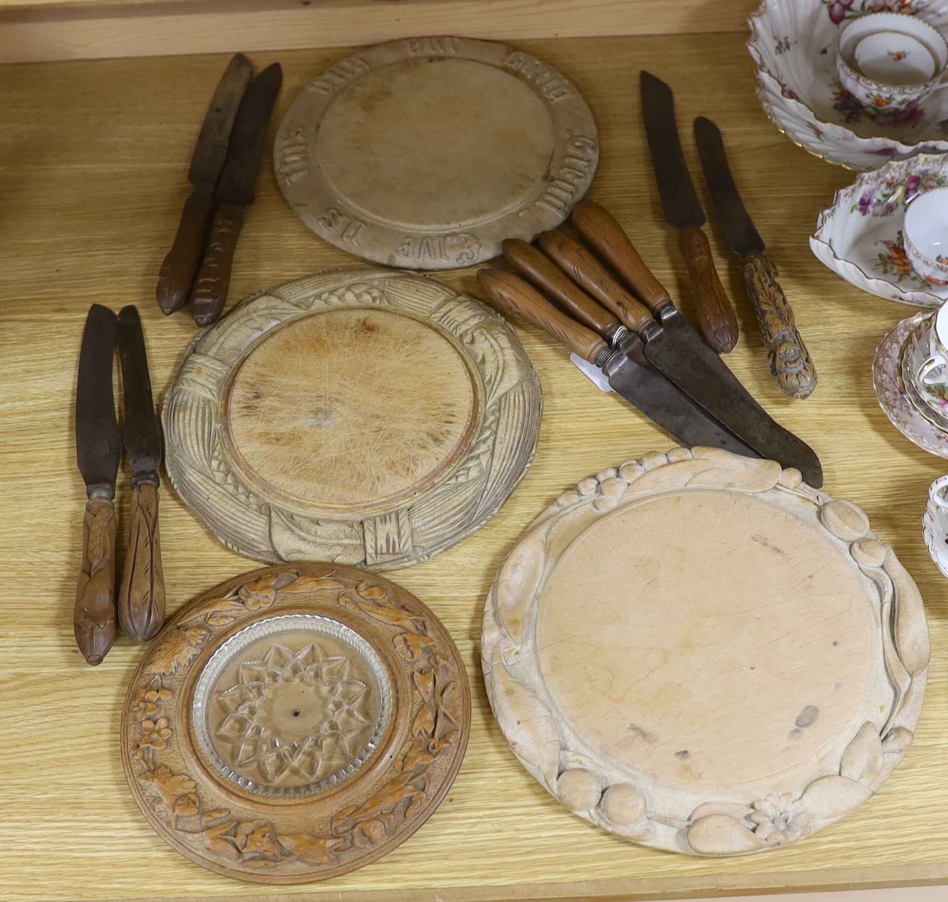 Three carved wood breadboards, a butter dish and a collection of knives with carved handles, largest 29cm in diameter